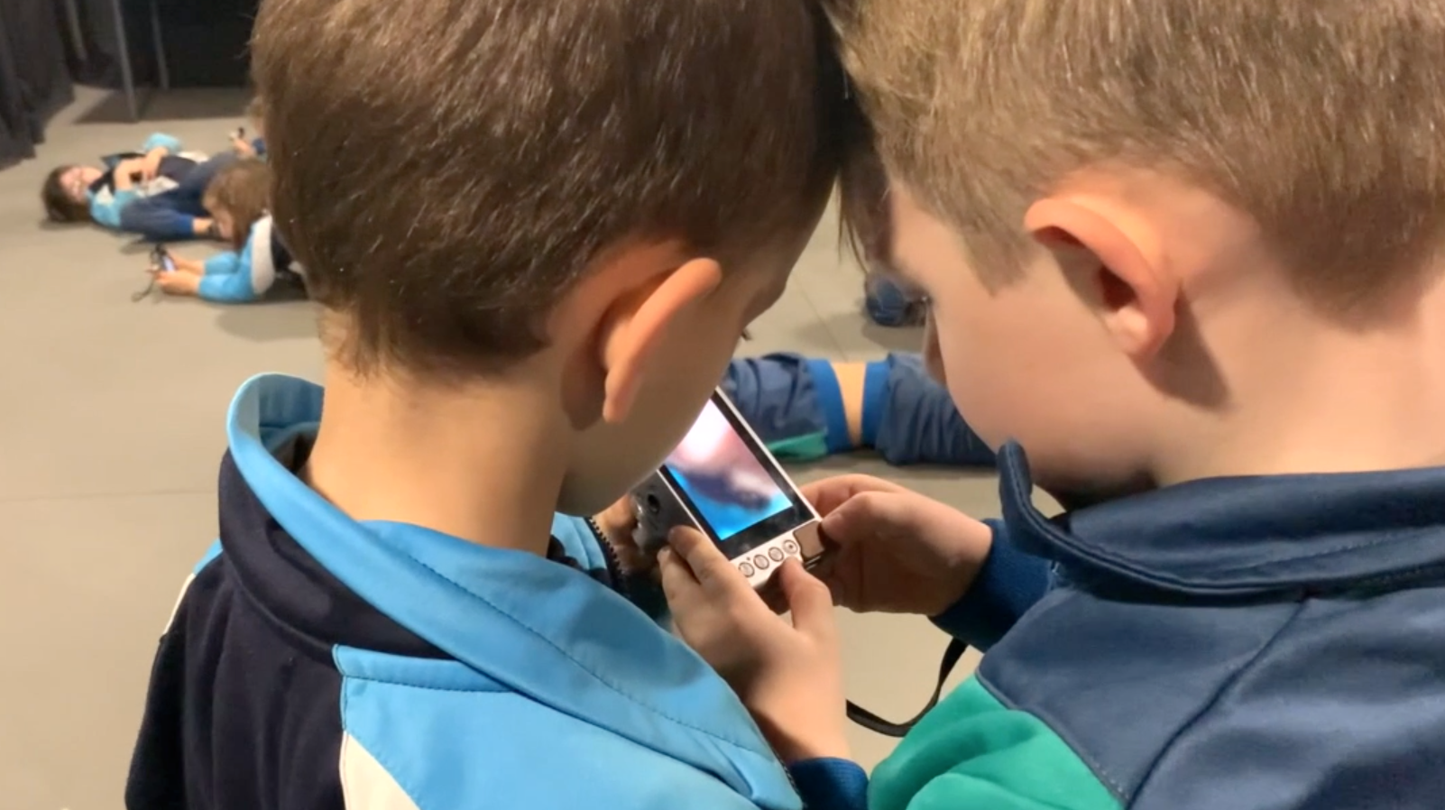 Contaplano de dos niños con las cabezas pegadas mirando juntos la pantalla de una cámara de fotos digital