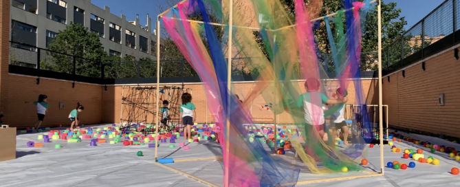 Instalación artística con niños jugando entre telas y piezas de distintos colores